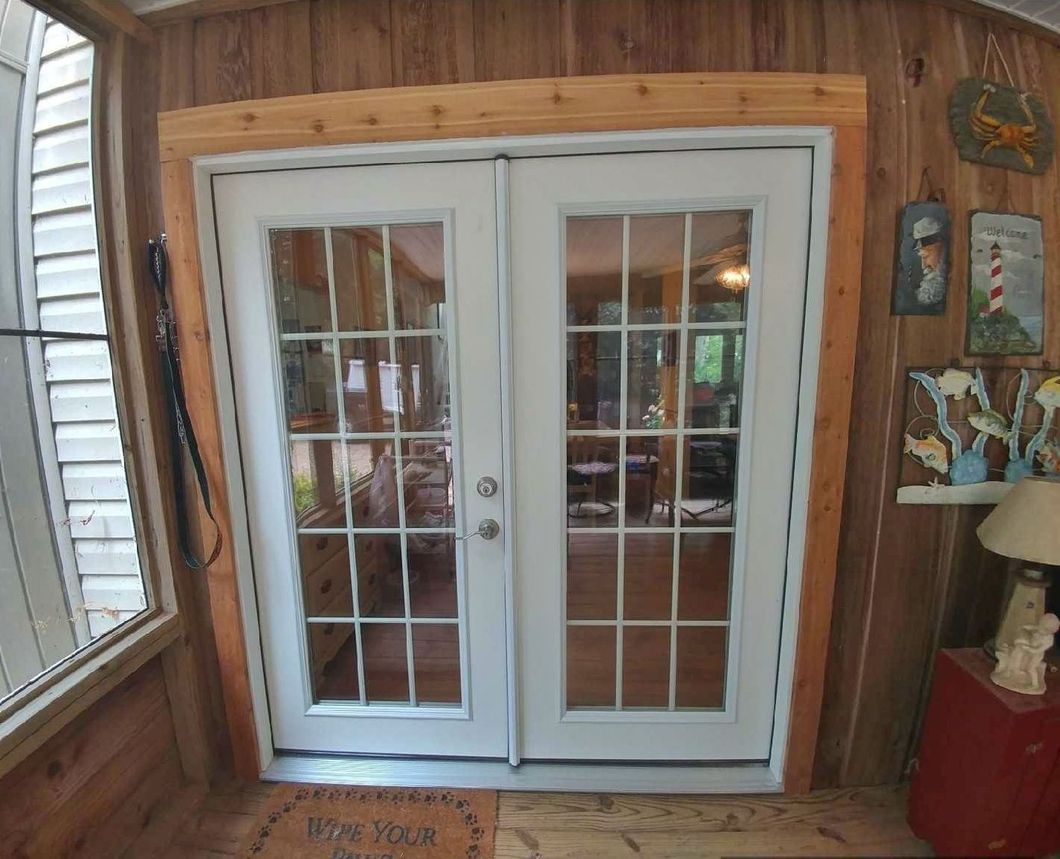 White French doors with glass panels, wooden frame, leading outside from a wood-paneled room.