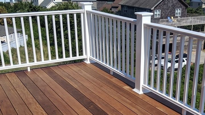 White railing on a wooden deck with a view of a house and trees in the background.