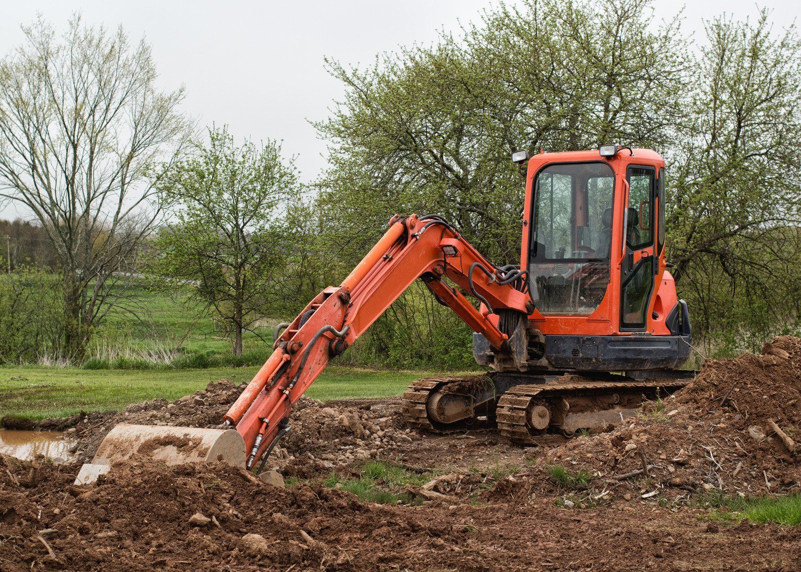 Orange excavator digging in dirt, in a field setting.
