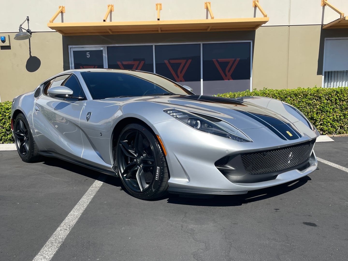 Silver Ferrari with black racing stripes parked outside a building.