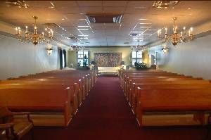 Empty church interior with wooden pews, red carpet, and chandeliers leading to the altar