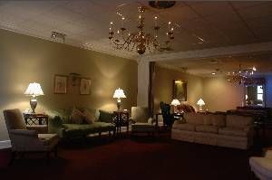 Dim hotel lounge with sofas, armchairs, lamps, and chandeliers in warm lighting.
