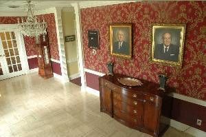 Elegant hallway with red patterned wallpaper, framed portraits, and a wooden sideboard on a marble floor.