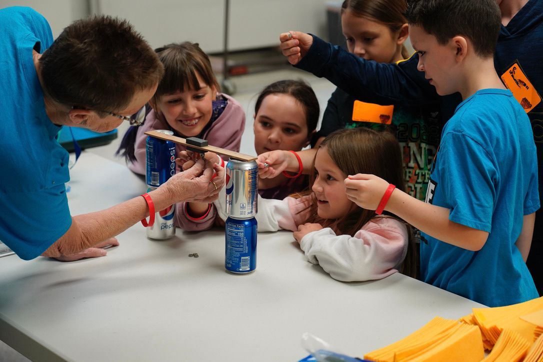 A group of children are sitting around a table playing with cans and sticks.