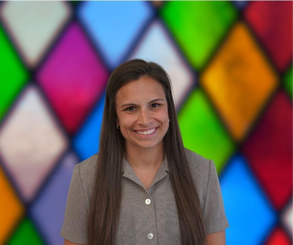 A woman is smiling in front of a stained glass window