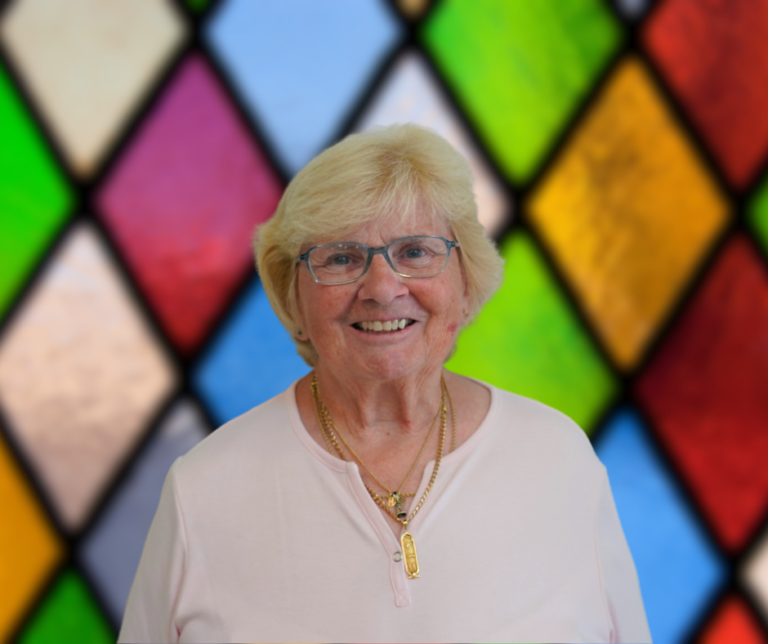 A woman wearing glasses is smiling in front of a stained glass window.