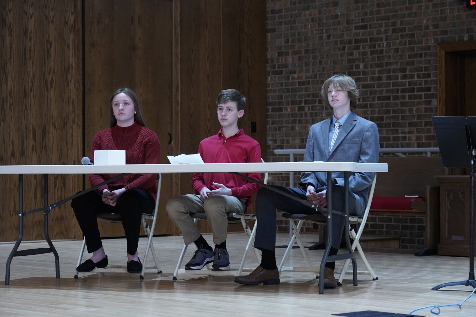 Three people are sitting at a table in front of a brick wall.
