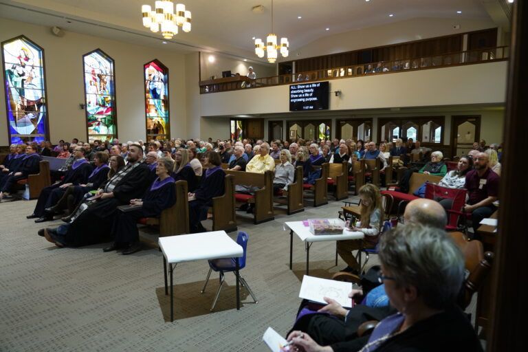 A large group of people are sitting in a church with stained glass windows