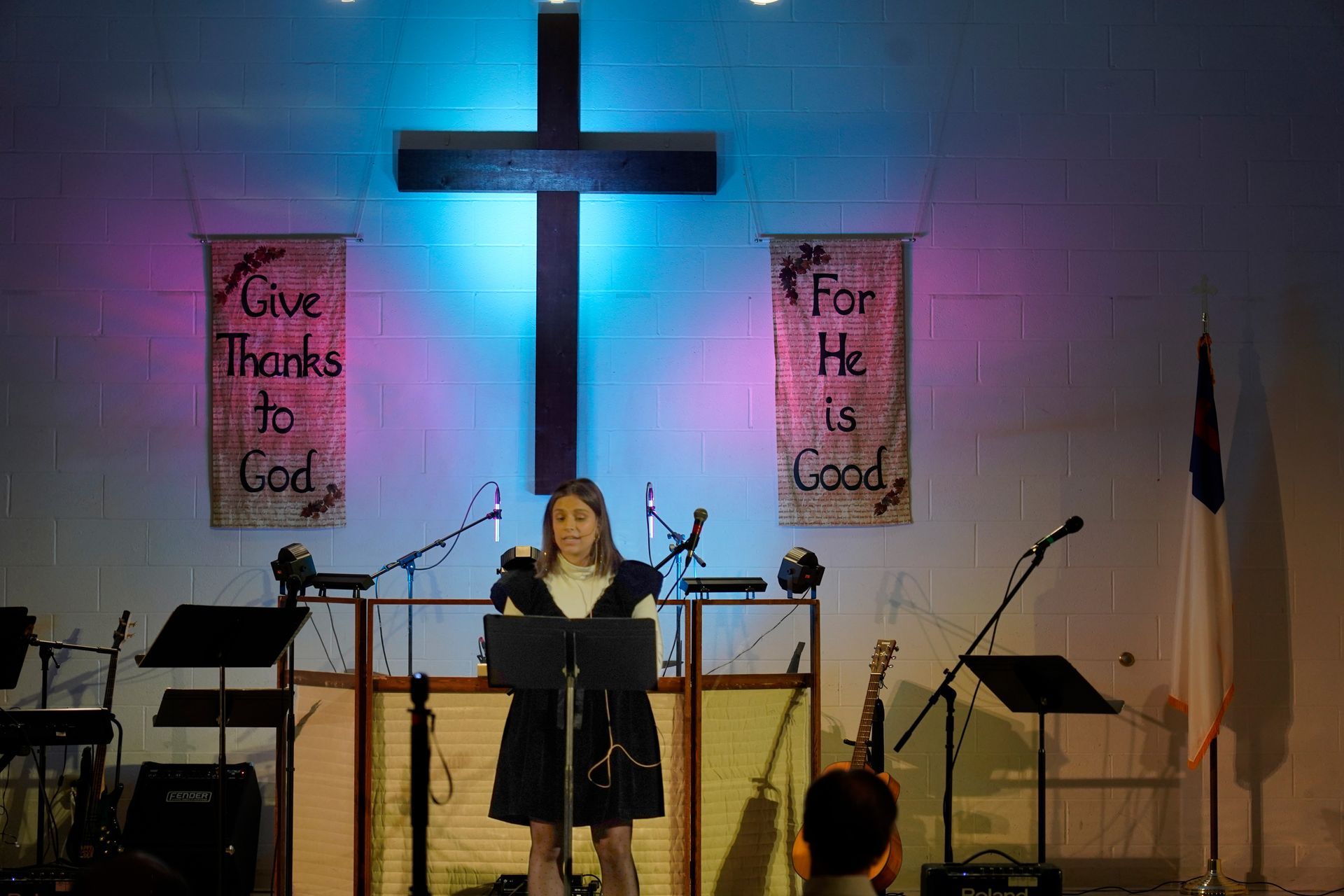 A woman is singing into a microphone in front of a cross in a church.