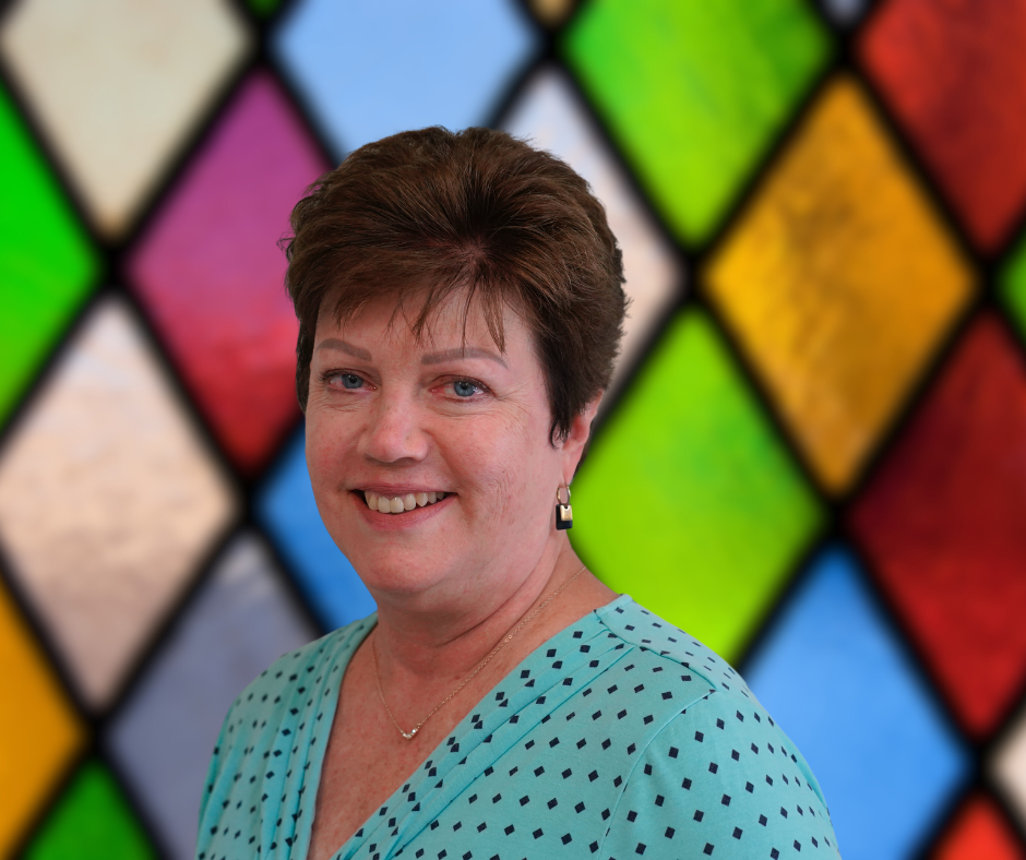 A woman is smiling in front of a stained glass window.
