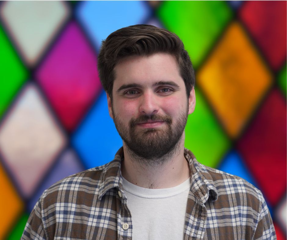 A man in a plaid shirt is standing in front of a stained glass window.