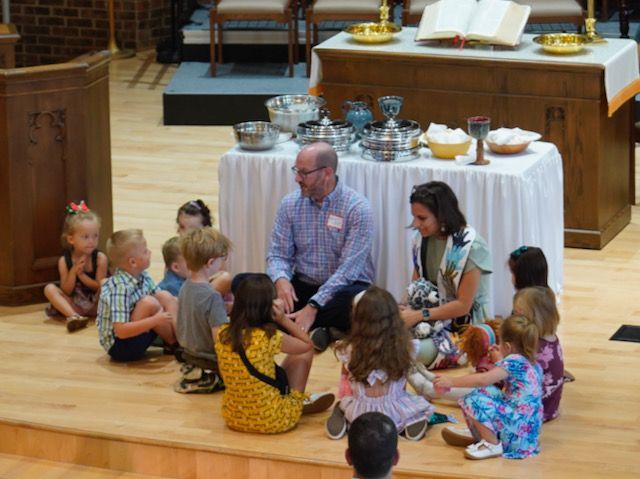 A group of children are sitting around a table in a church.