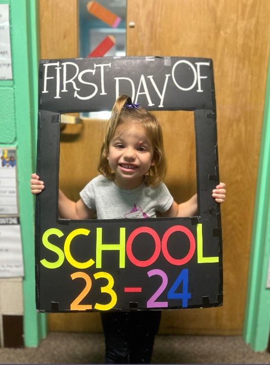 A little girl is holding a sign that says first day of school 23-24