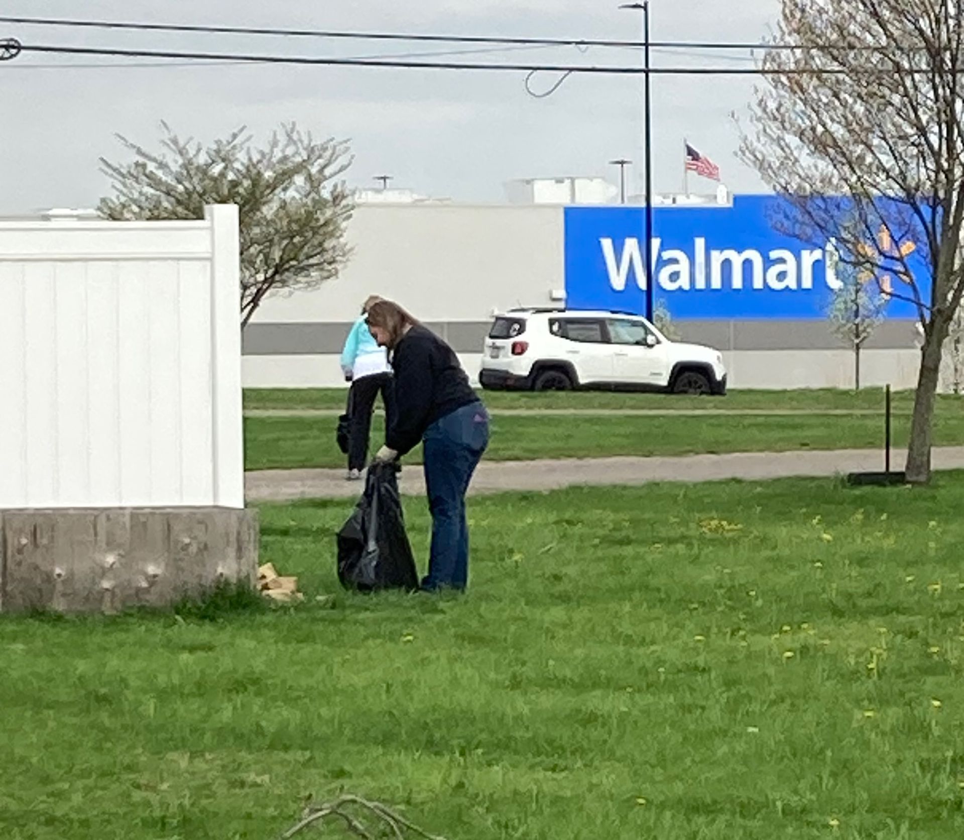 A woman is picking up trash in front of a walmart store