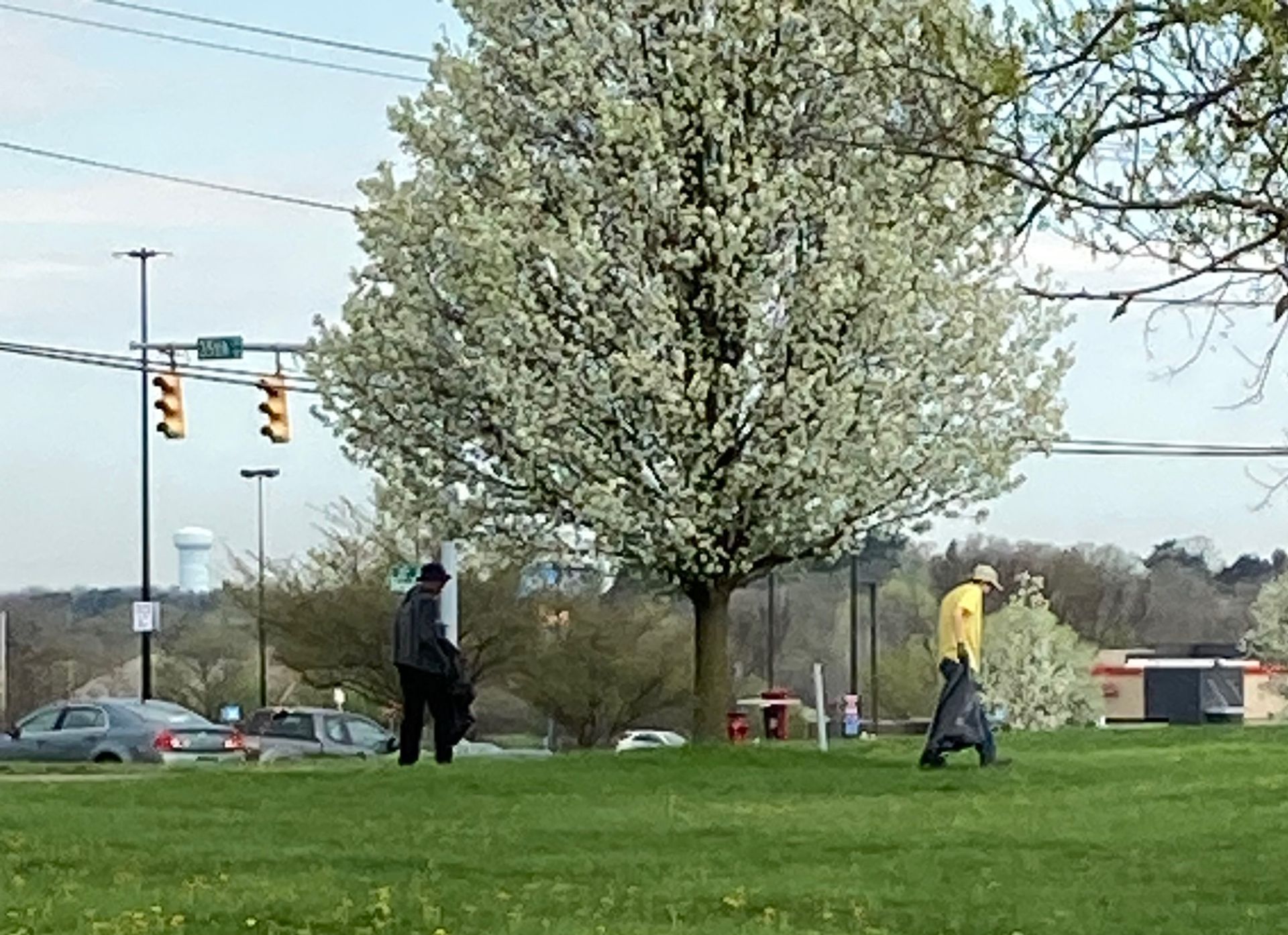 A man in a yellow shirt is pushing a golf cart in a park
