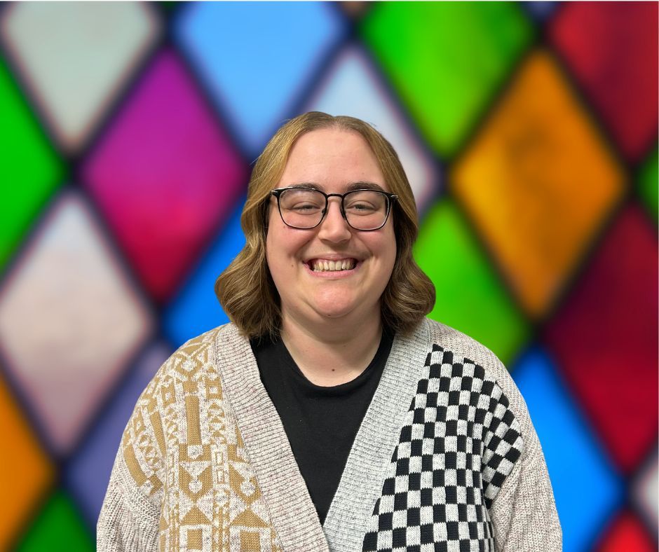 A woman is smiling in front of a stained glass window.