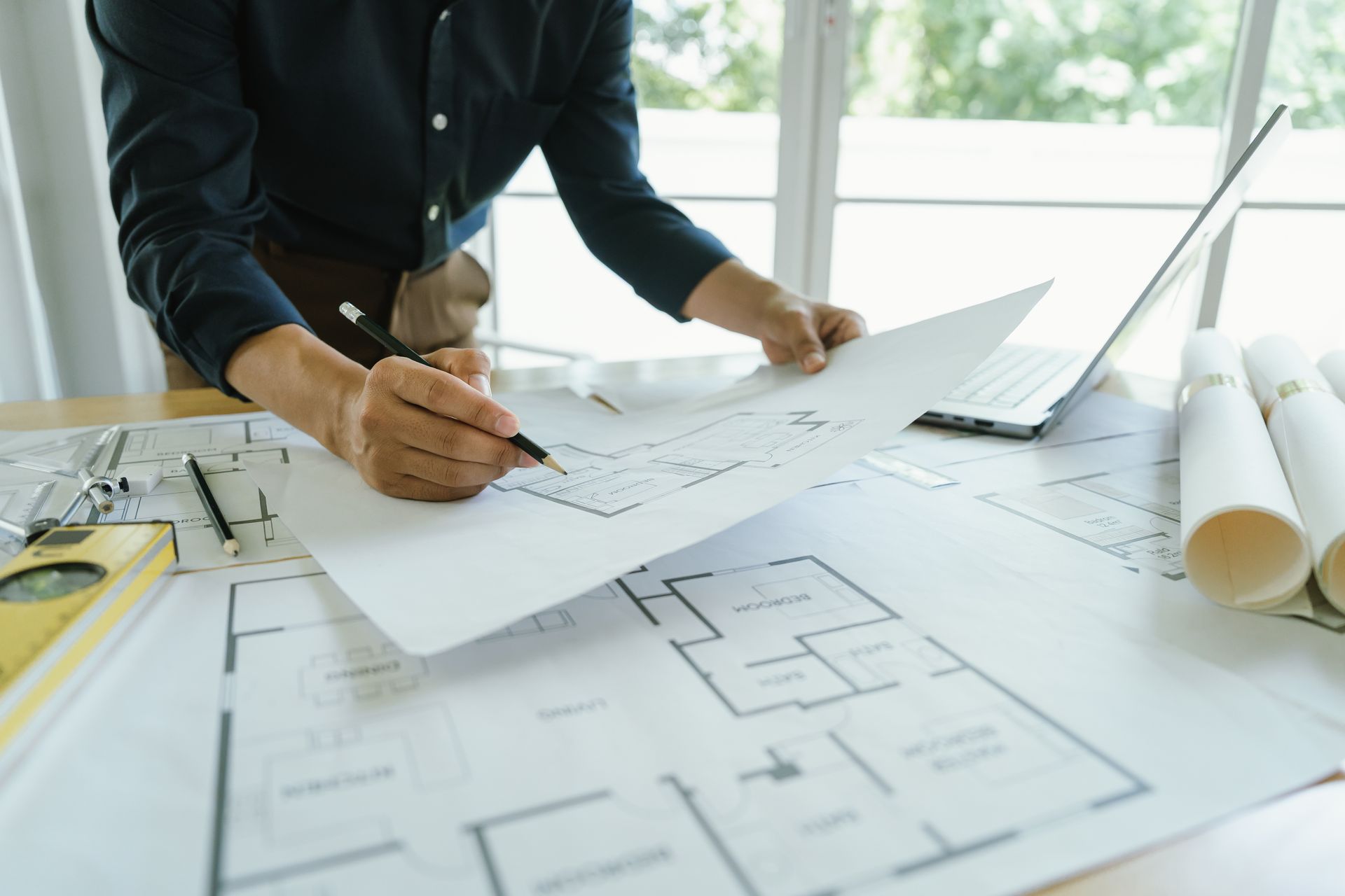 Architectural plans & detailed drawings spread out on a table, showcasing design elements & layout. Draftsman reviewing house drafting plans and floor plan drawings at a desk.