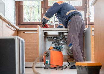A man is using a vacuum cleaner to clean a sink in a kitchen.