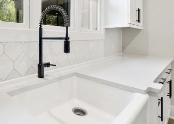 A kitchen sink with a black faucet and white cabinets.