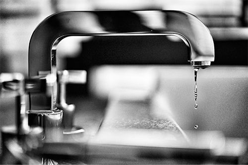 A black and white photo of a faucet with water dripping from it.