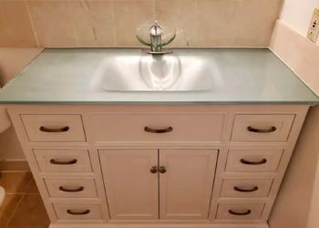 A bathroom vanity with a stainless steel sink and a glass counter top.