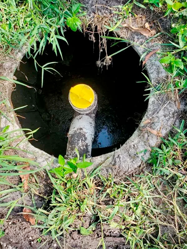 A drain hole in the ground with a yellow cap on it.