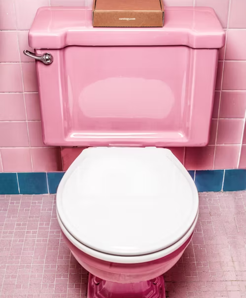 A pink toilet with a box on top of it in a bathroom.