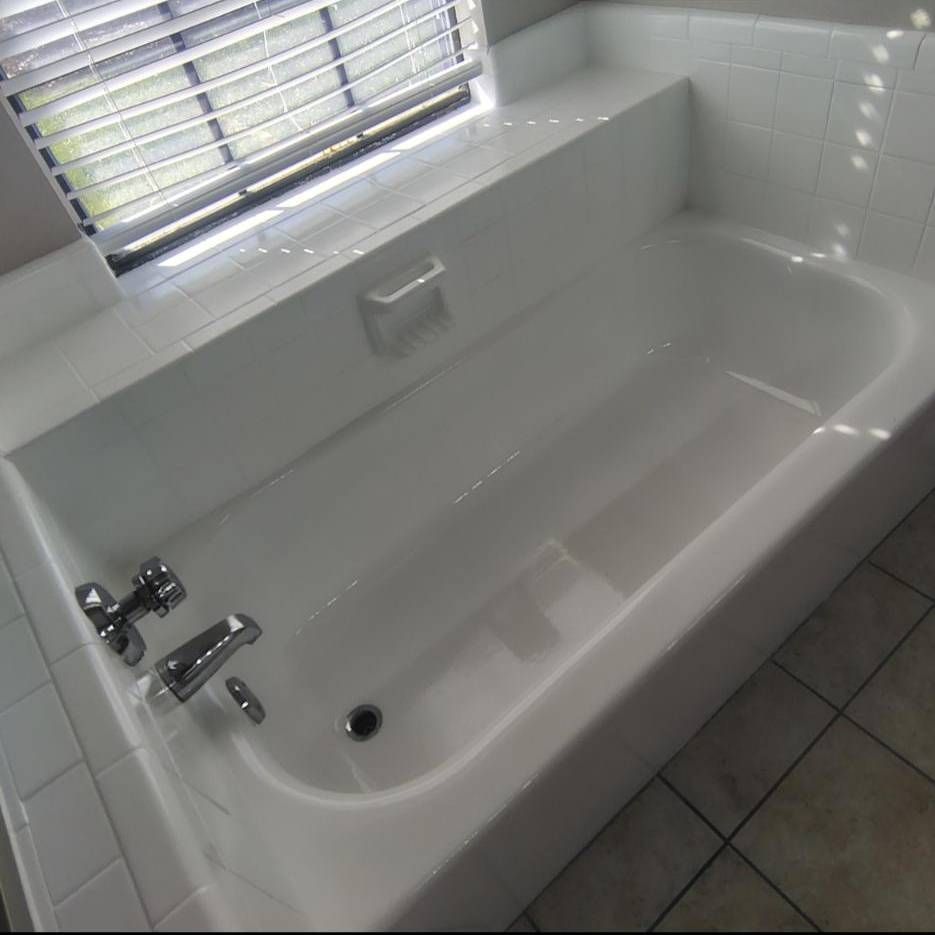 A white bathtub with chrome fixtures, located in a tiled bathroom beneath a window with blinds.