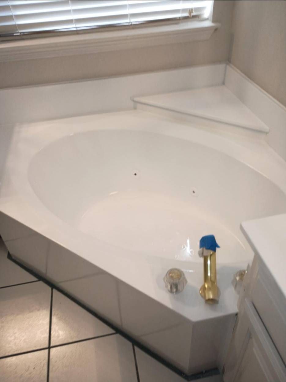 A white, built-in soaking tub with chrome fixtures in a corner tiled bathroom with white window blinds.