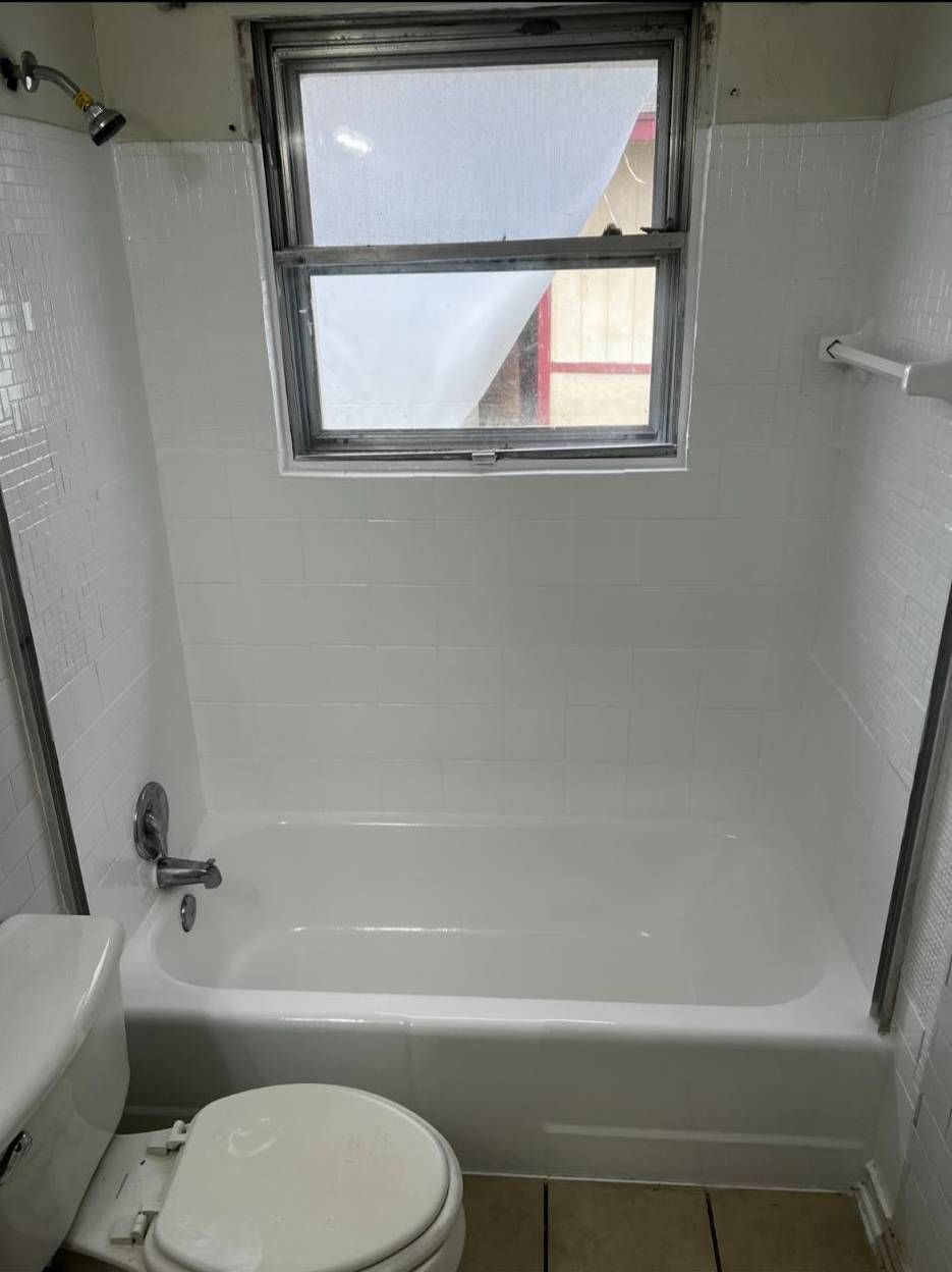 A white bathtub and shower surround with white tiled walls and a single window centered above the tub.