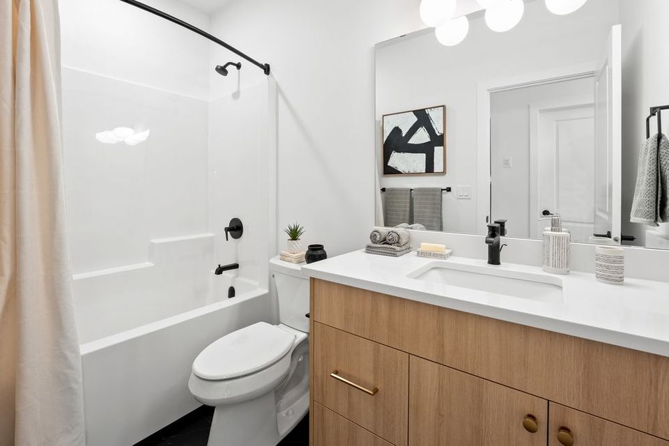 Modern bathroom with white tub, toilet, vanity, and wood cabinets under bright lights