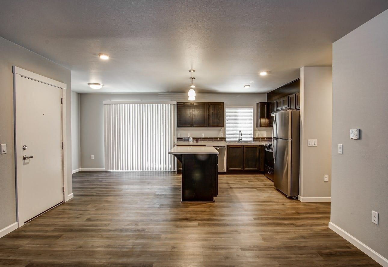 Empty modern kitchen and living area with wood floors, dark cabinets, and sliding glass doors