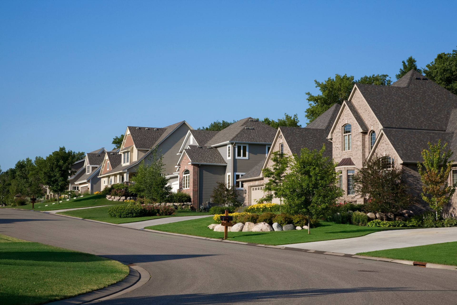 Suburban street with houses, green lawns, and blue sky.