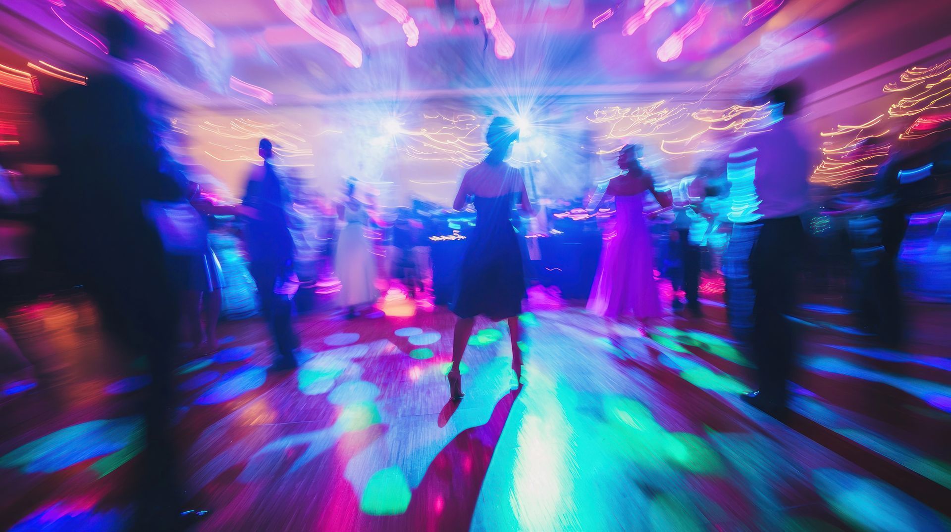 Blurred dancers under neon pink and blue lights on a glowing dance floor at a wedding event