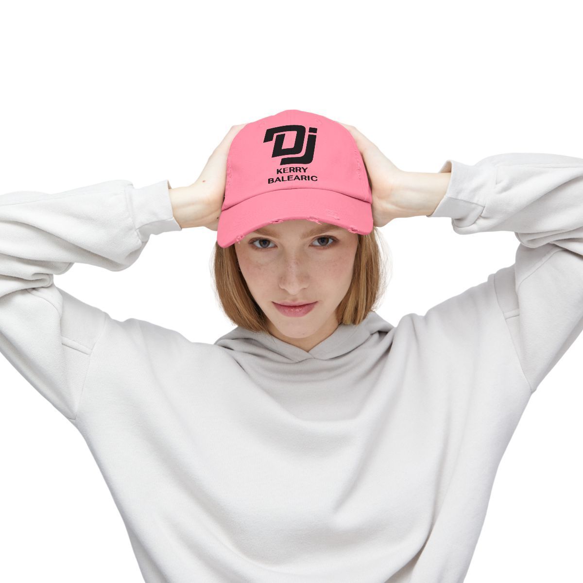 Person in a white sweatshirt adjusting a pink DJ Kerry Balearic cap, facing forward on a plain white background