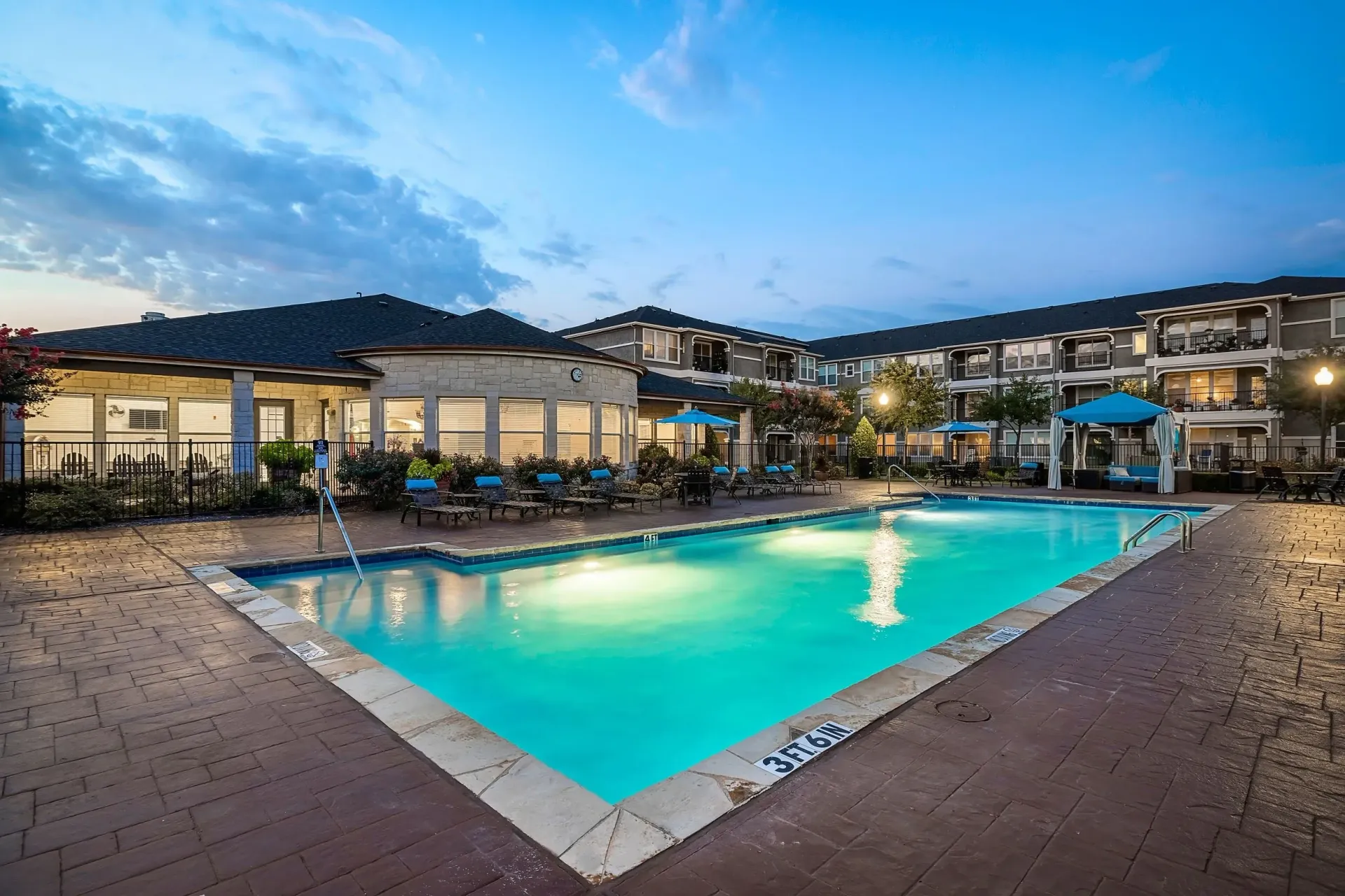 Outdoor swimming pool with lounge chairs and cabanas at dusk.
