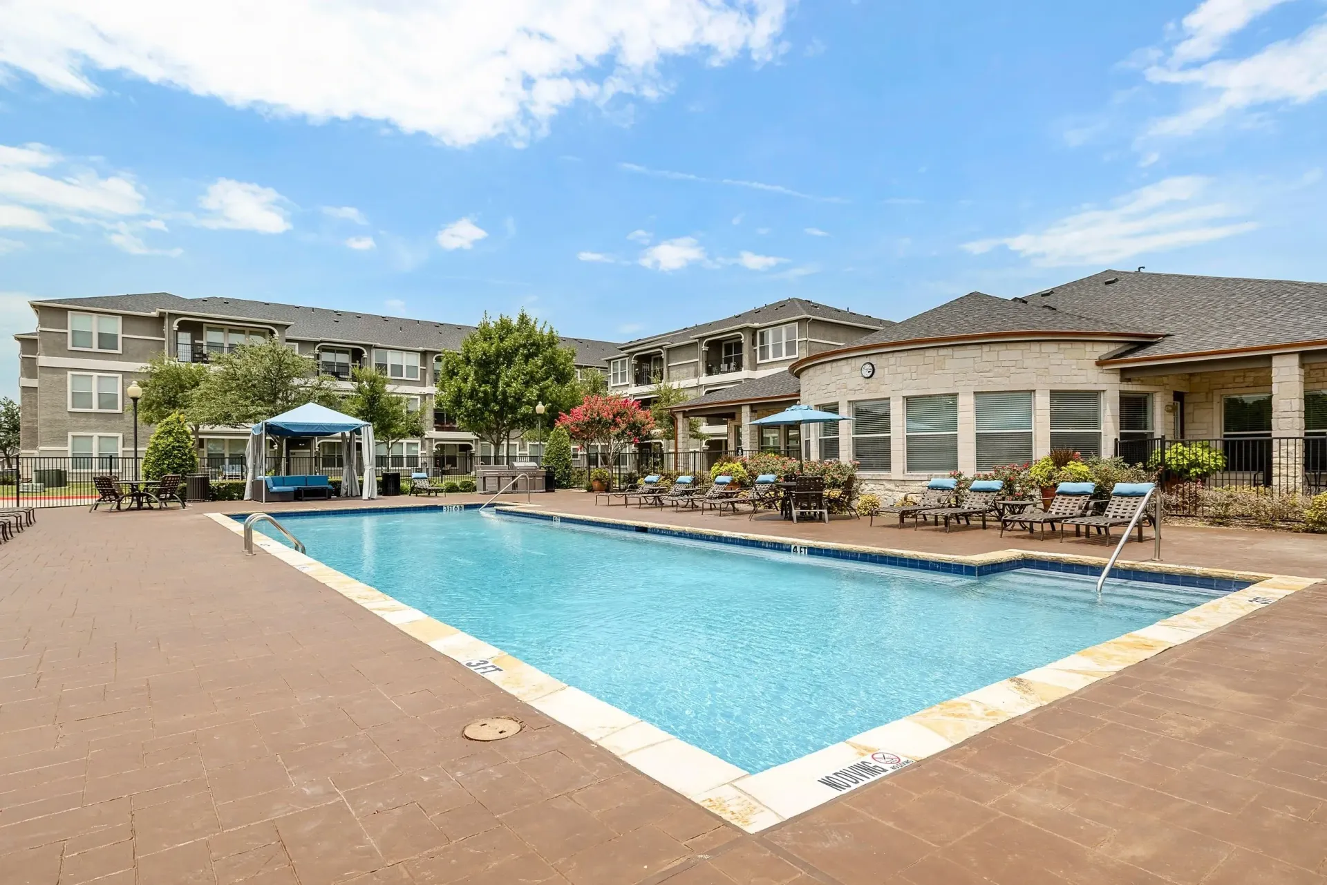 Resort-style swimming pool with lounge chairs and cabana at apartment complex.