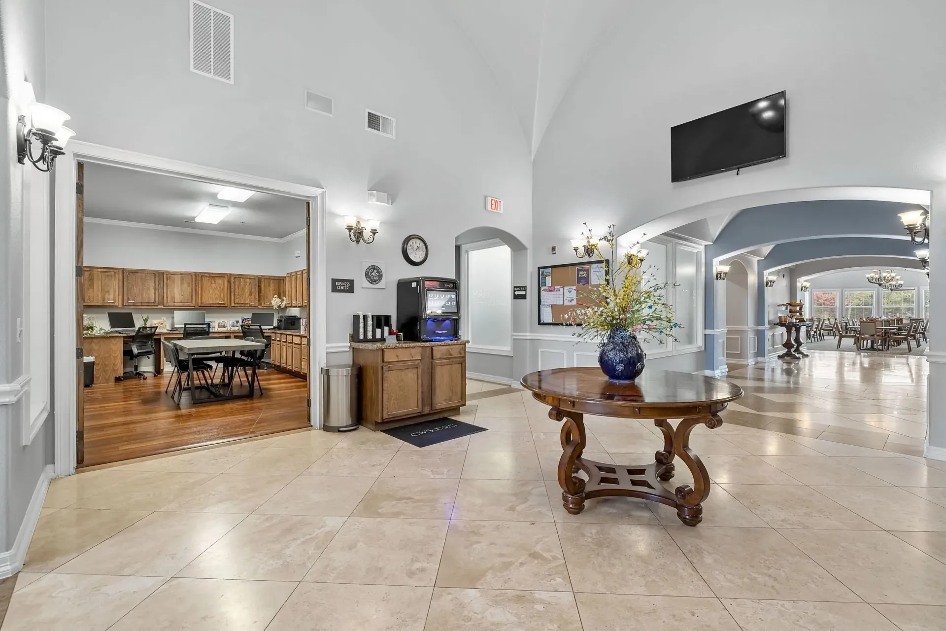 Elegant lobby with a round wooden table, coffee station, and view into a business center.