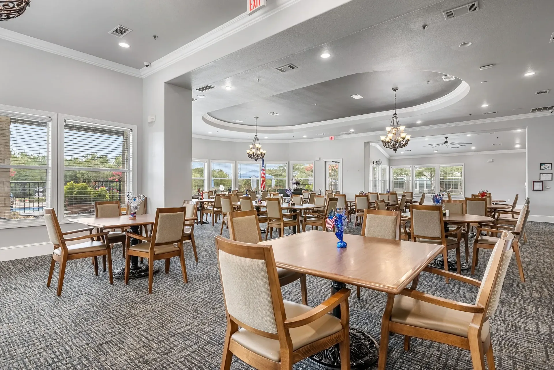 Dining hall with tables and chairs, view of outdoor pool through window.