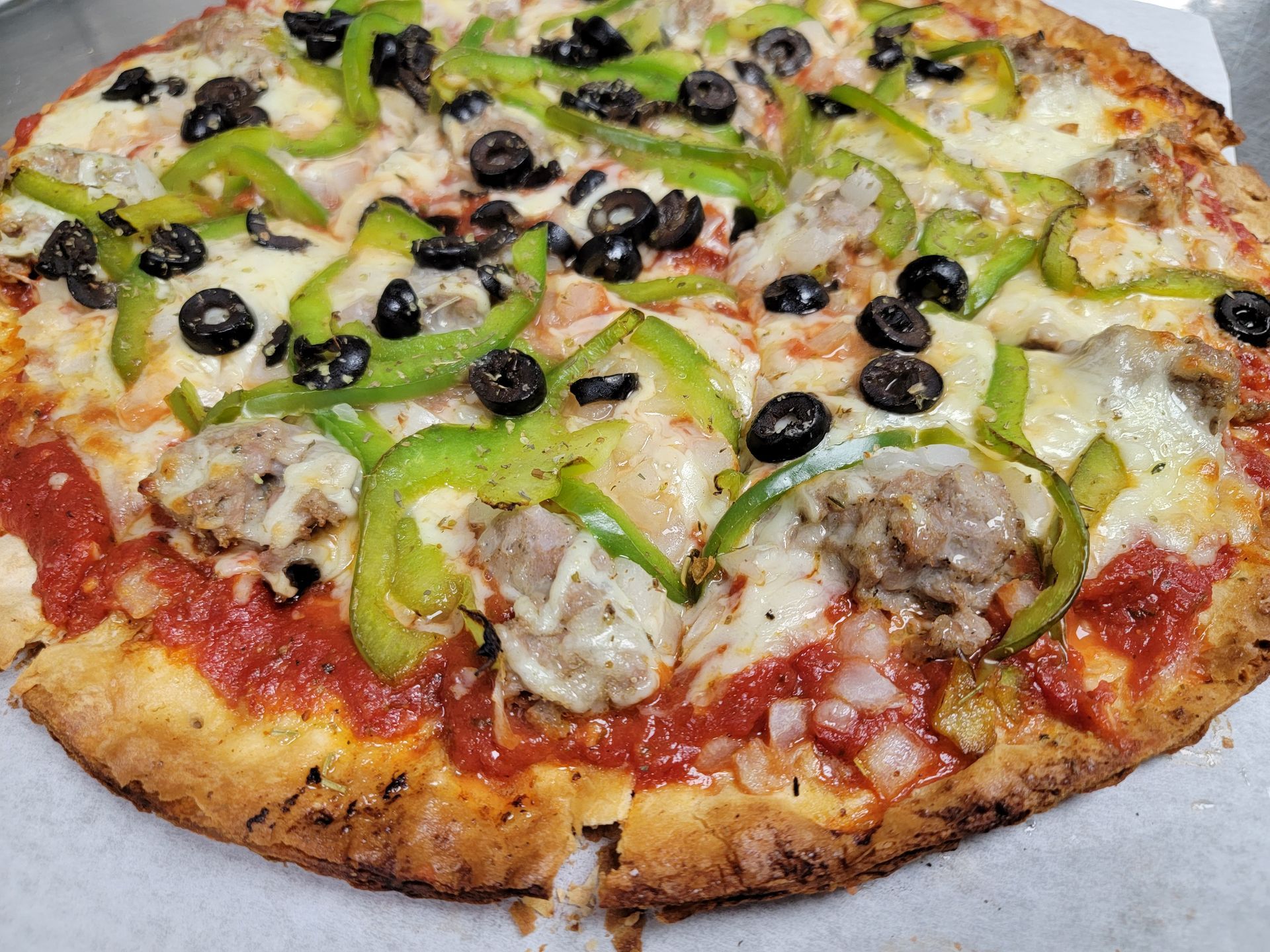 A pizza with peppers , olives , sausage and cheese is sitting on a table.