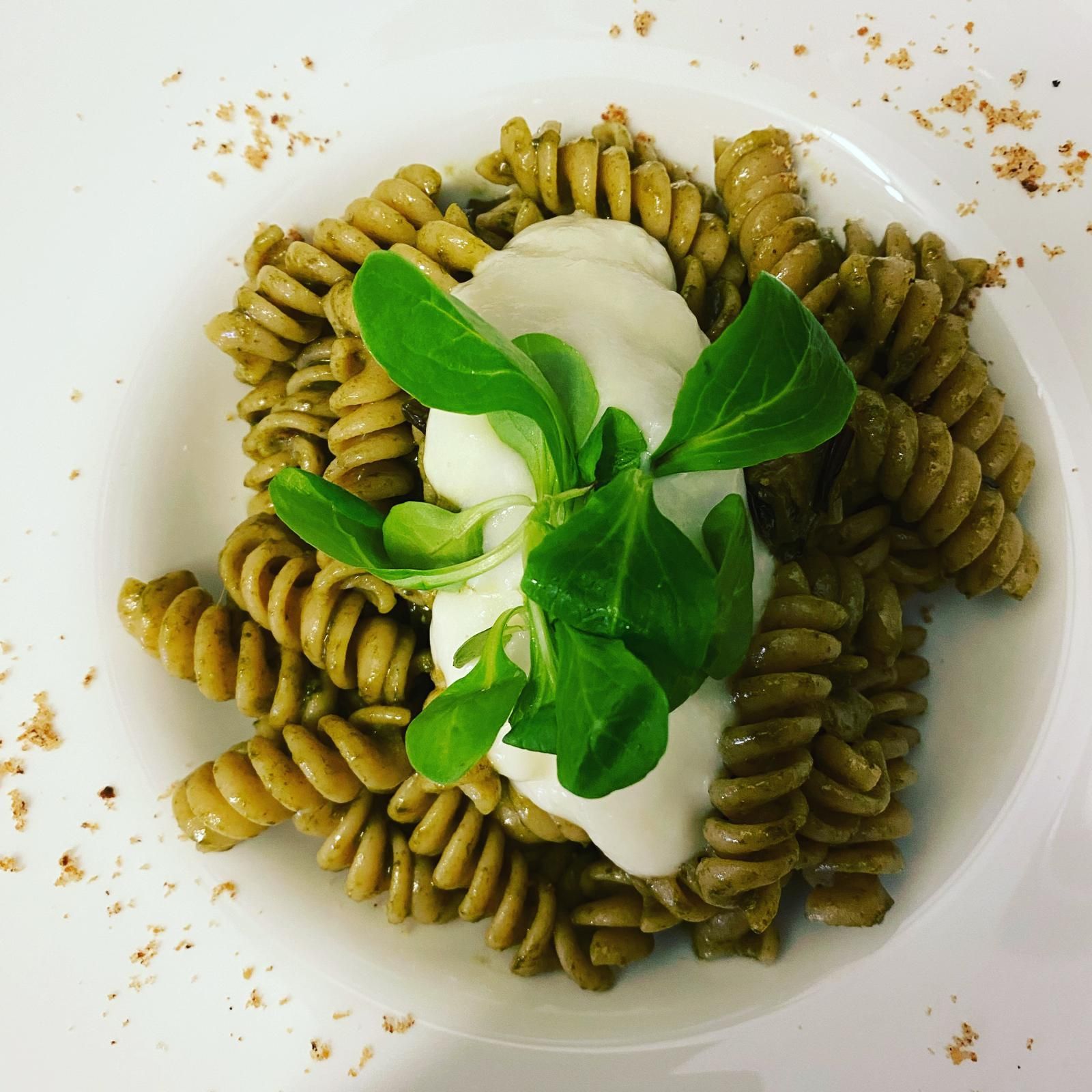 Pasta verde a spirale con salsa bianca e foglie verdi su un piatto bianco.
