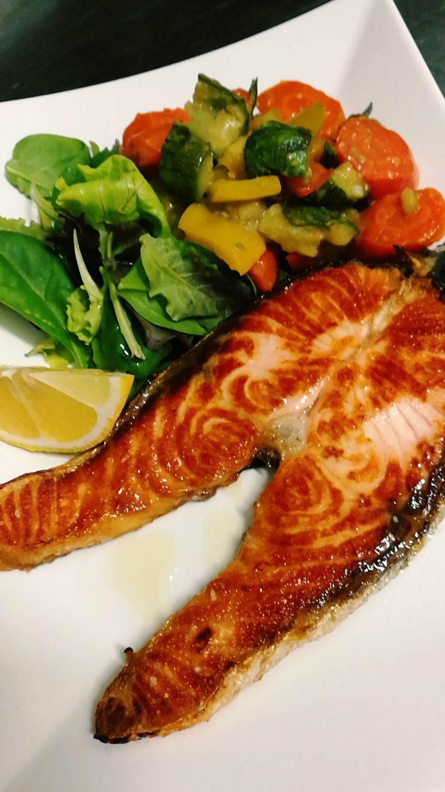 Salmone alla griglia con verdure e insalata su un piatto bianco.