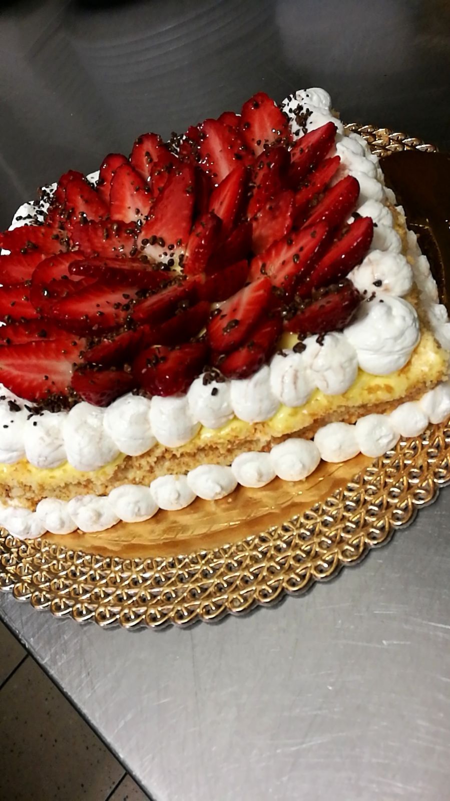 Torta di pasta frolla alle fragole su un piatto d'oro, con strati di panna montata e guarnita con semi.