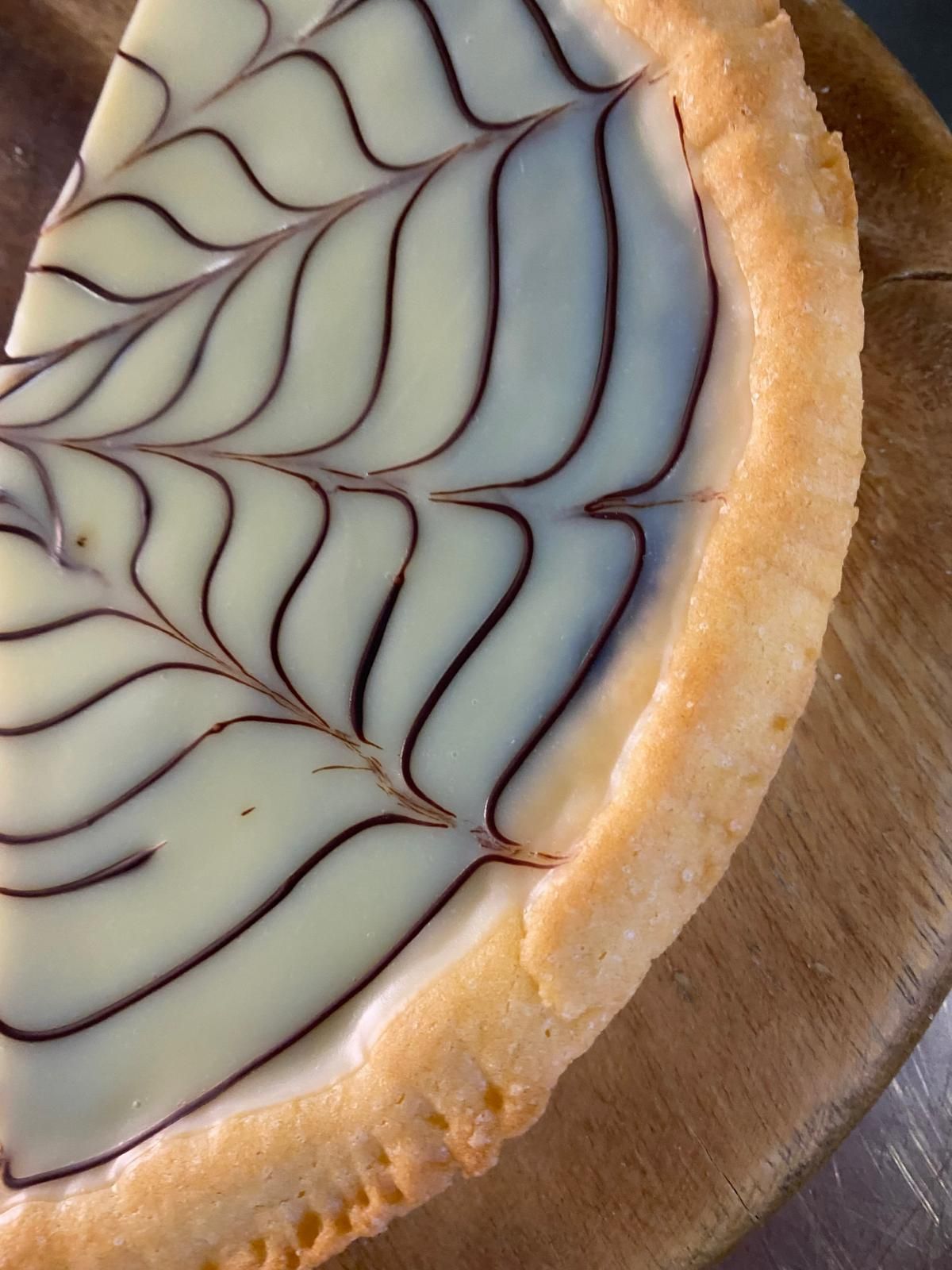 Fetta di crostata con glassa bianca e spirale di cioccolato fondente, su una superficie di legno.