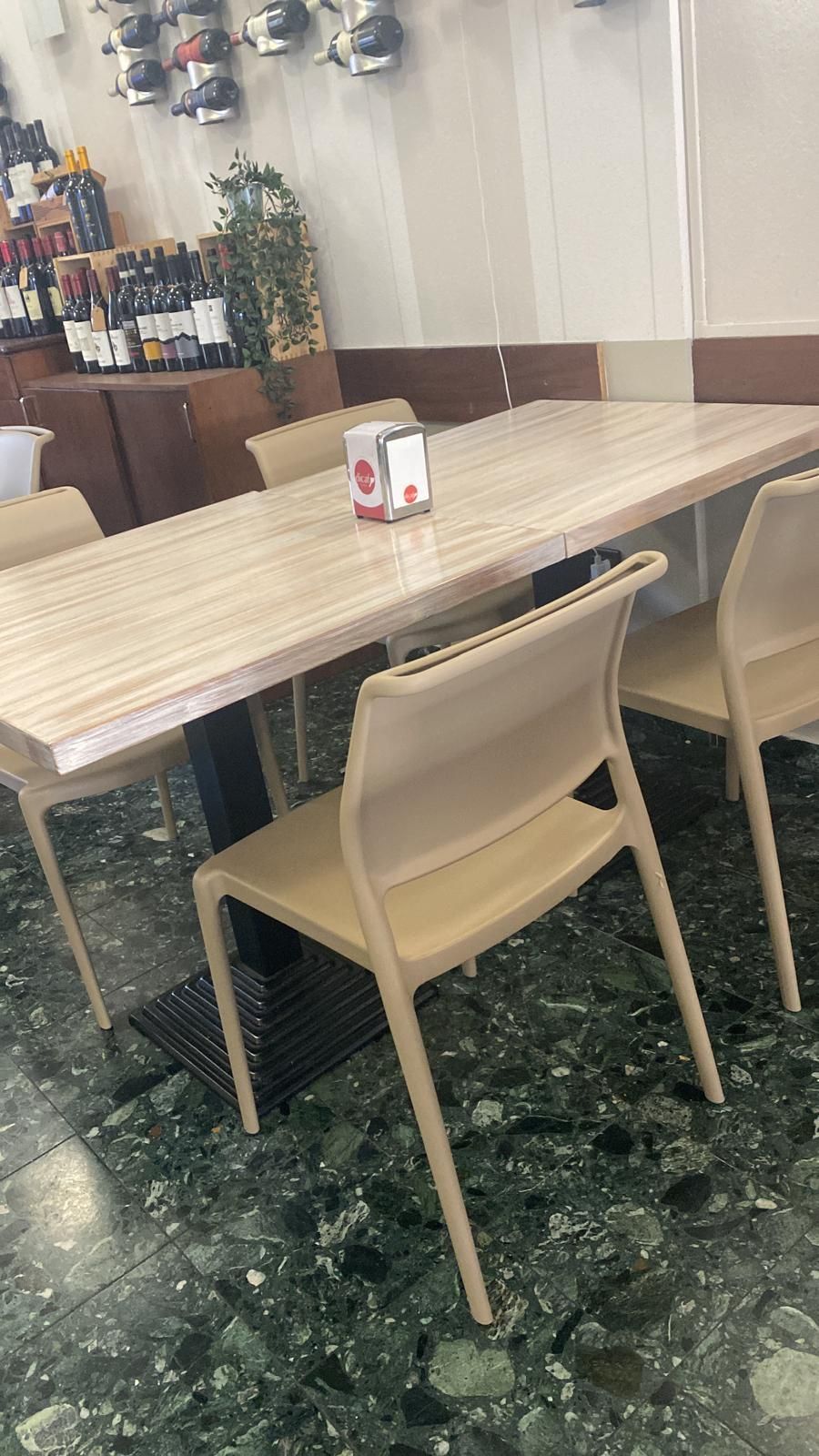 Un tavolo da ristorante con quattro sedie. Bottiglie di vino sullo sfondo, pavimento piastrellato verde e nero.