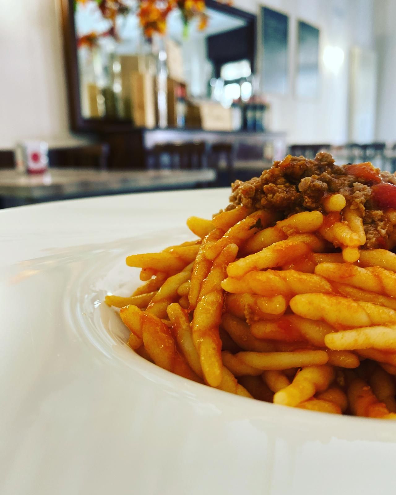 Piatto di pasta con sugo di carne in una ciotola bianca, ambientazione di un ristorante.