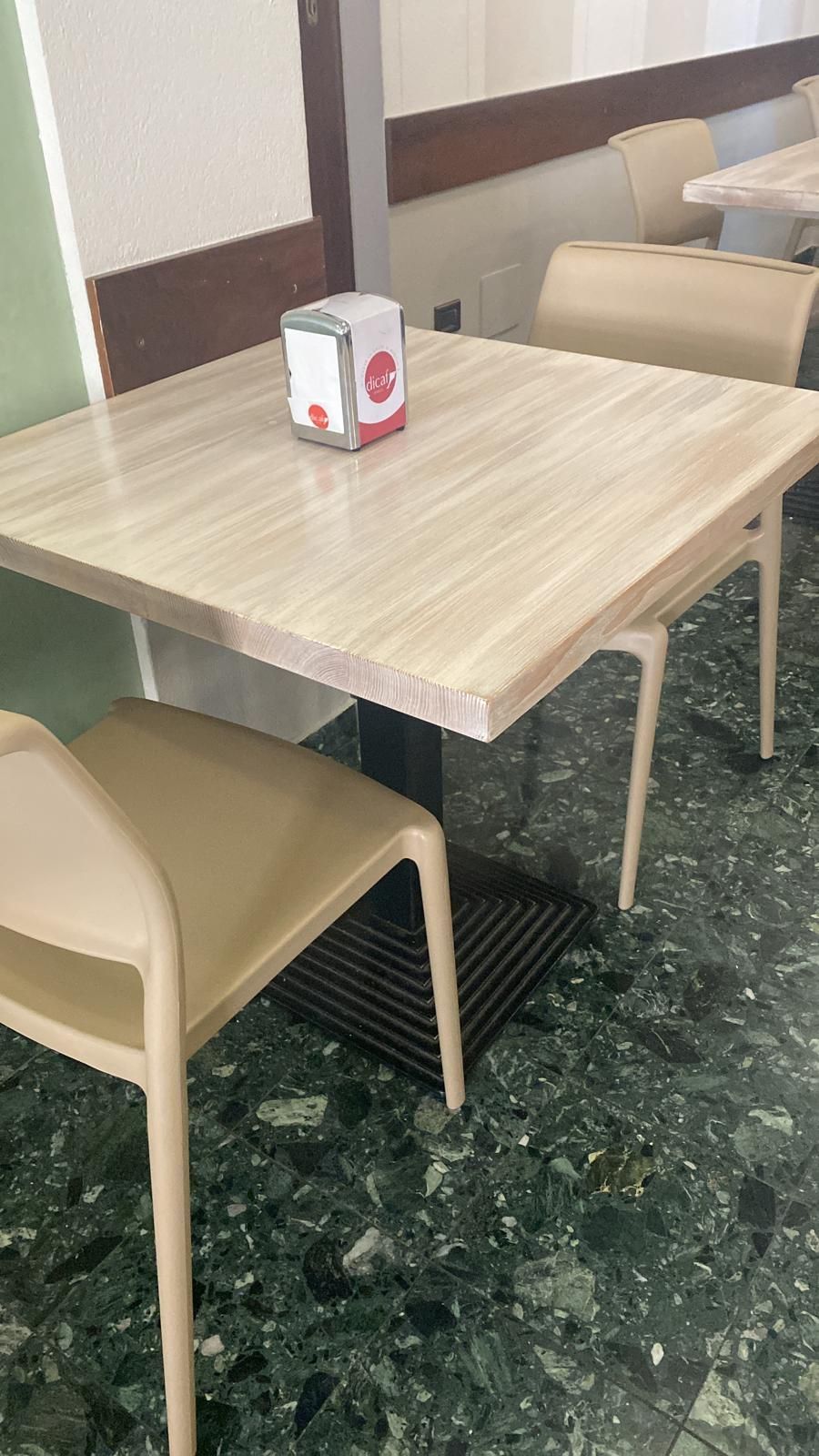 Un tavolo quadrato con due sedie beige in un ambiente da bar, sul tavolo c'è un porta tovaglioli.