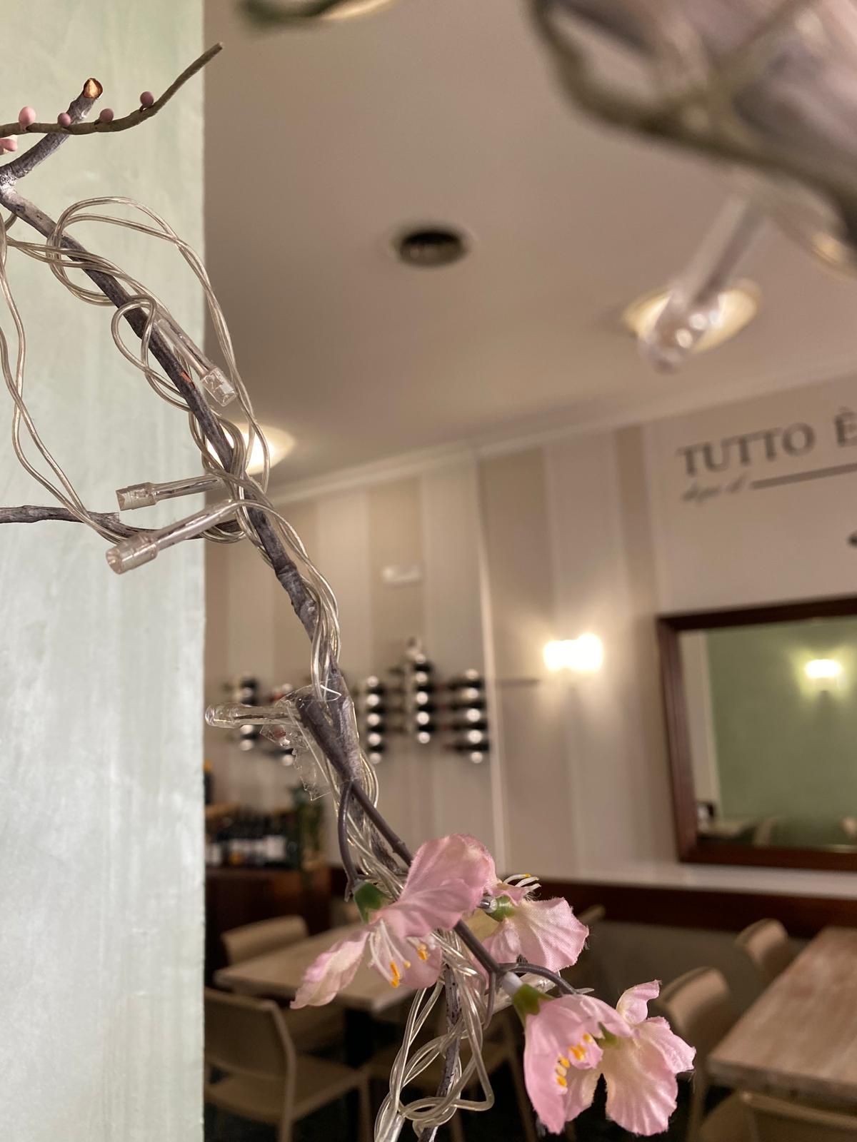 Primo piano di fiori rosa su rami argentati in un bar con pareti neutre e uno specchio.