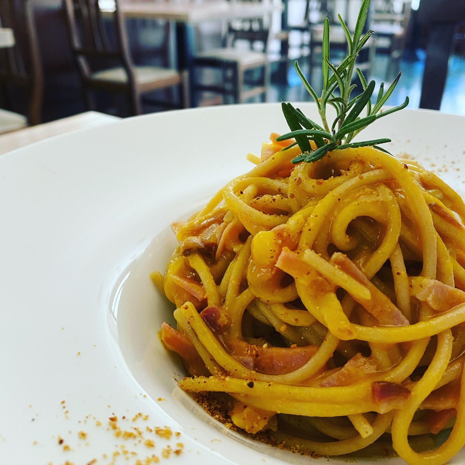 Piatto di pasta con salsa cremosa e pancetta, guarnito con rosmarino, servito su un piatto bianco.