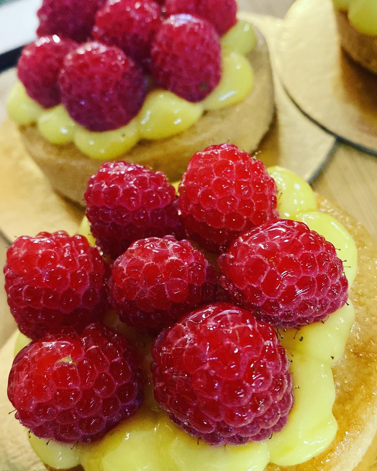 Crostatine ai lamponi: lamponi rossi freschi su un ripieno di crema pasticcera gialla, in una crosta dorata.